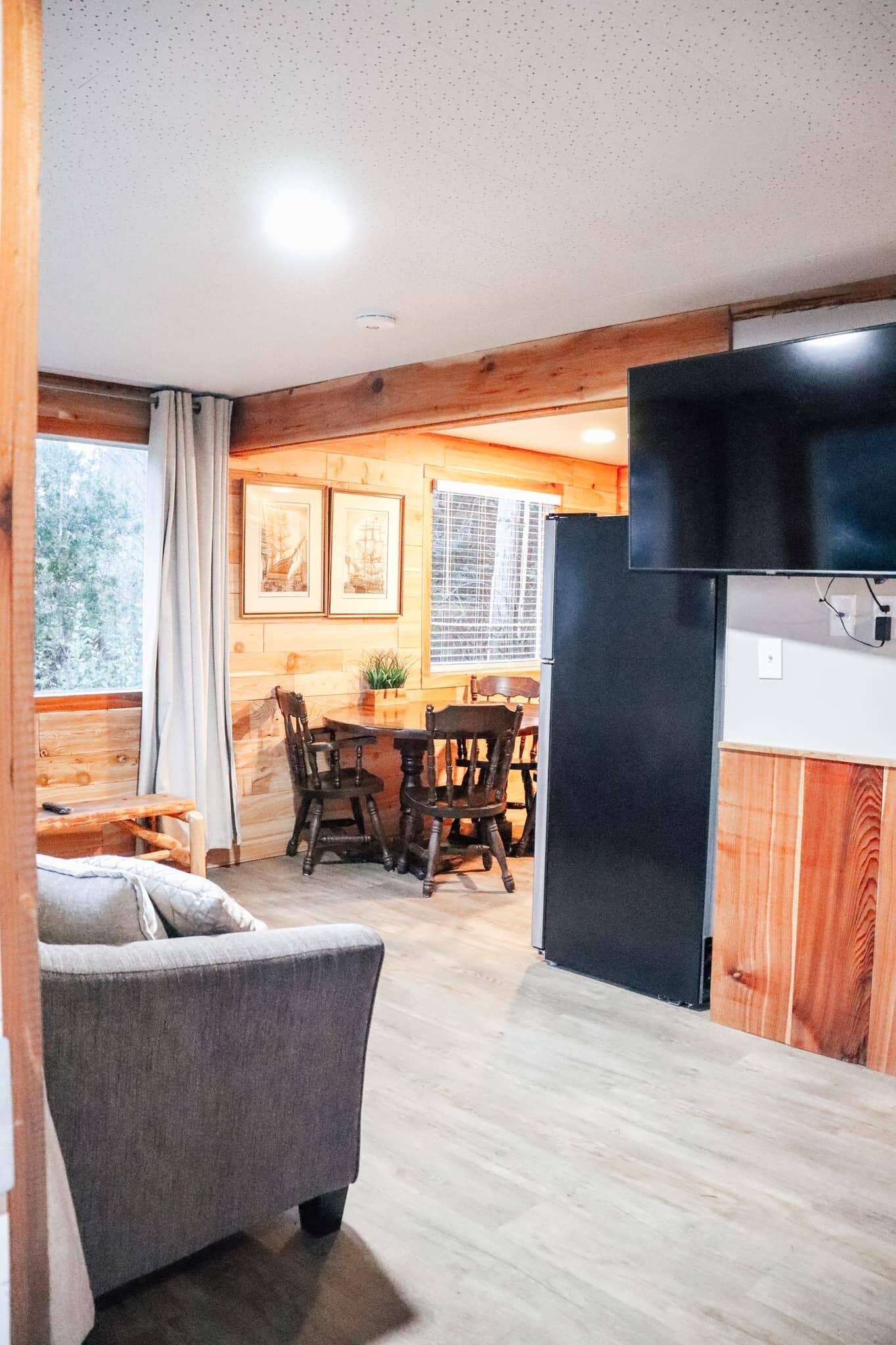 A cozy cabin interior with a dining area, a sofa, and a TV mounted on a wooden wall.