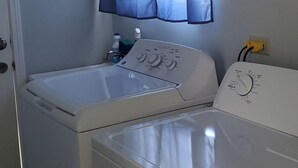 A laundry room with two white washing machines and a window with blue curtains. - Luxry Seaview House by the Ocean (Lucea)
