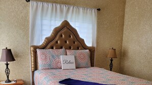 A bedroom with a tufted headboard, patterned bedding, a bedside table with lamps, a bench, and a decorative rug. - Luxry Seaview House by the Ocean (Lucea)