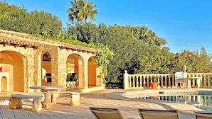 Uma área à beira da piscina com arcos de pedra, espreguiçadeiras e piscina.