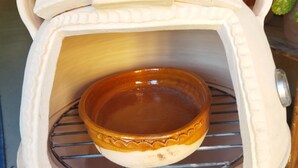 Un horno de cerámica con una rejilla metálica en su interior, colocado sobre un soporte.