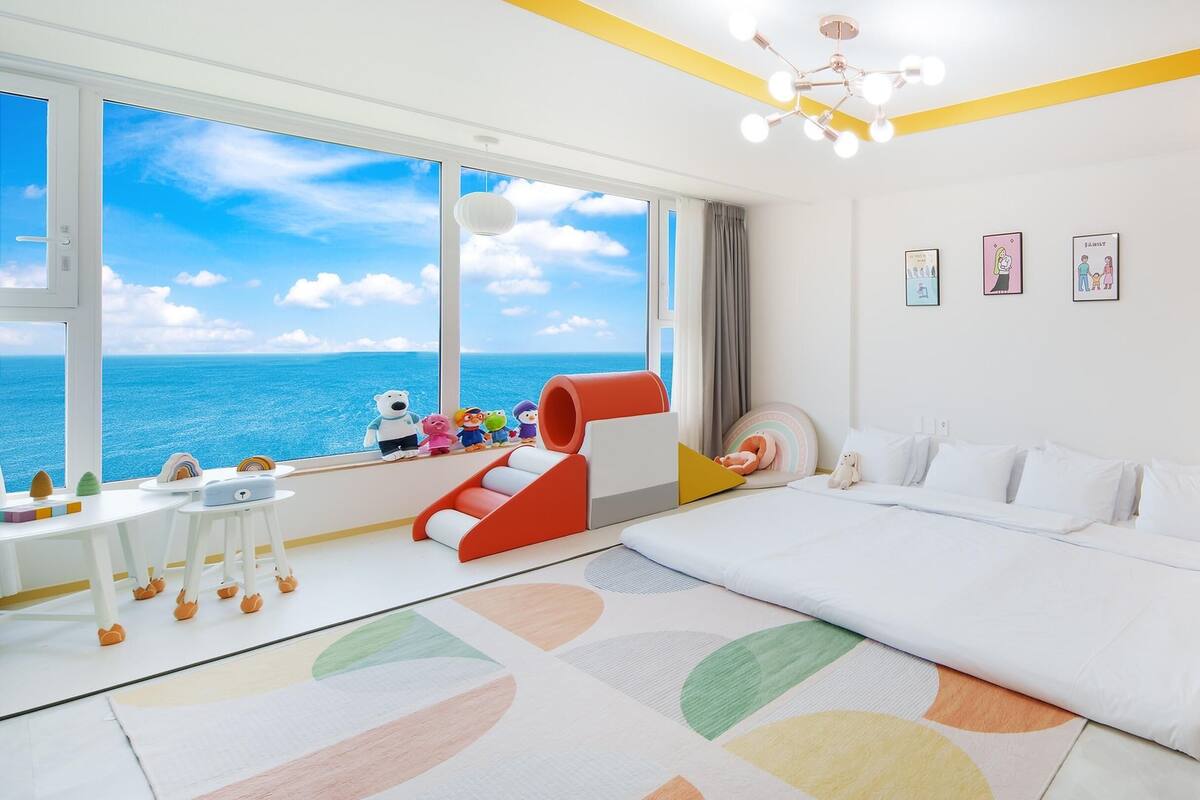 Ein modernes Schlafzimmer mit einem großen Bett, einem Schreibtisch mit Spielzeug und Blick auf den Ozean.