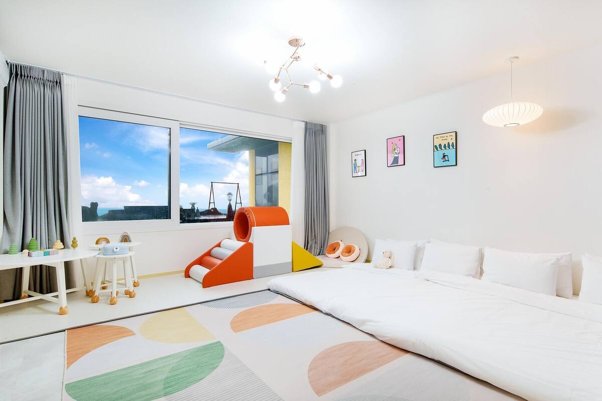 Ein helles, modernes Schlafzimmer mit einem großen Bett, einem Schreibtisch und einem Fenster mit Meerblick.
