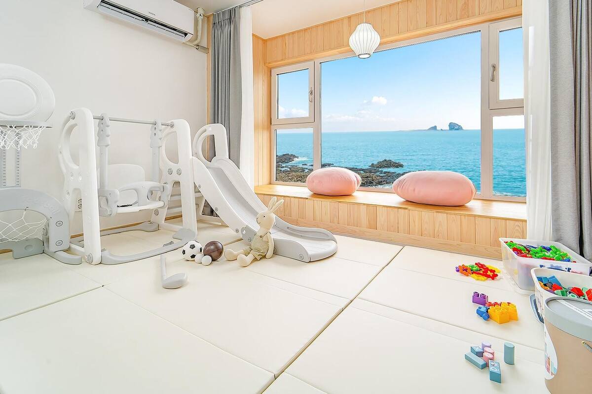 Ein Kinderspielbereich mit Rutsche, Spielzeug und einem Fenster mit Meerblick.