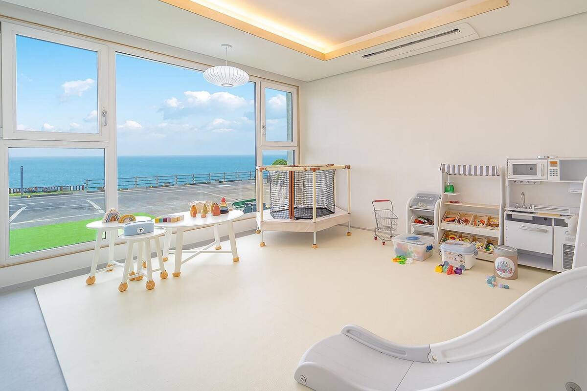 Ein heller, moderner Raum mit großen Fenstern und einem reizvollen Ausblick, einem Spielbereich mit Spielzeug und einer Küchenzeile.