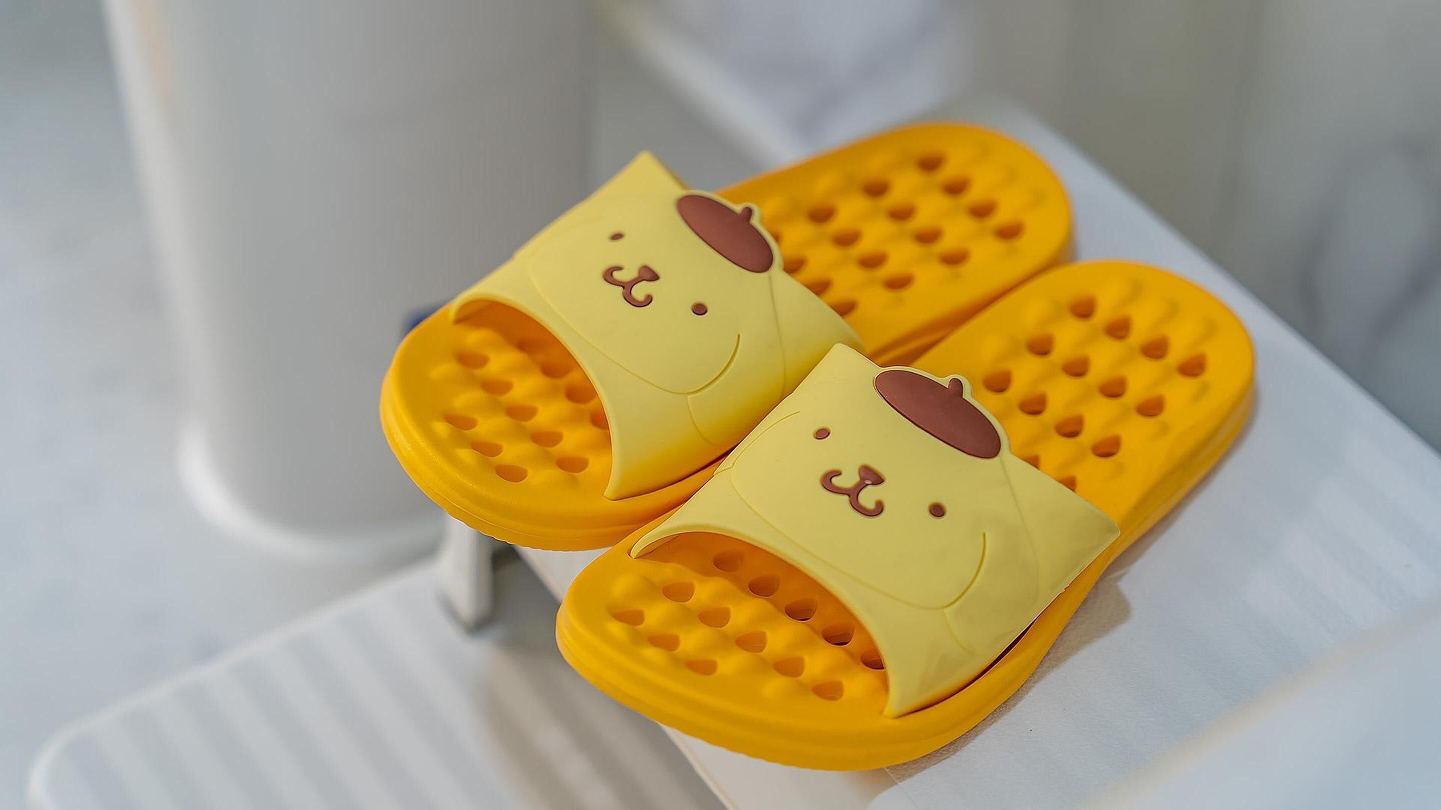 A pair of yellow slippers with a smiling face design.
