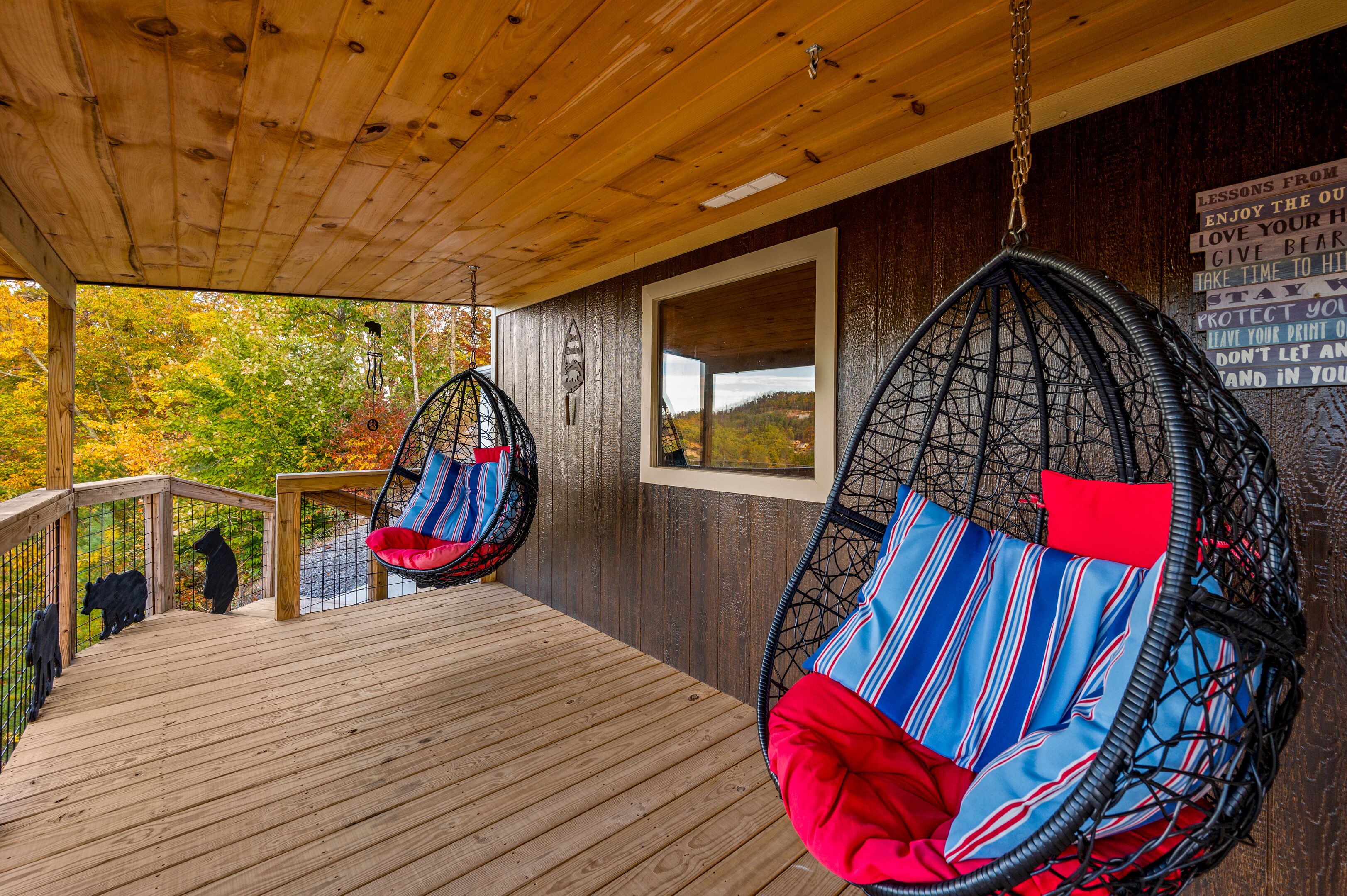 A wooden deck with two hanging chairs, a wooden railing, and a view of autumn foliage.