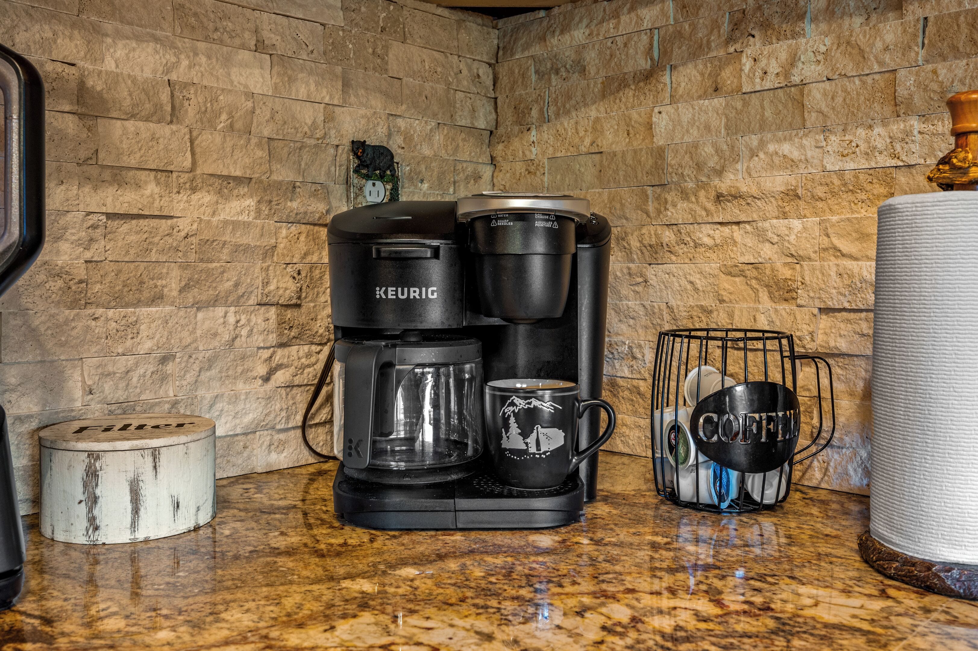 Una cafetera, una taza, un recipiente para café y un filtro sobre una encimera de cocina.