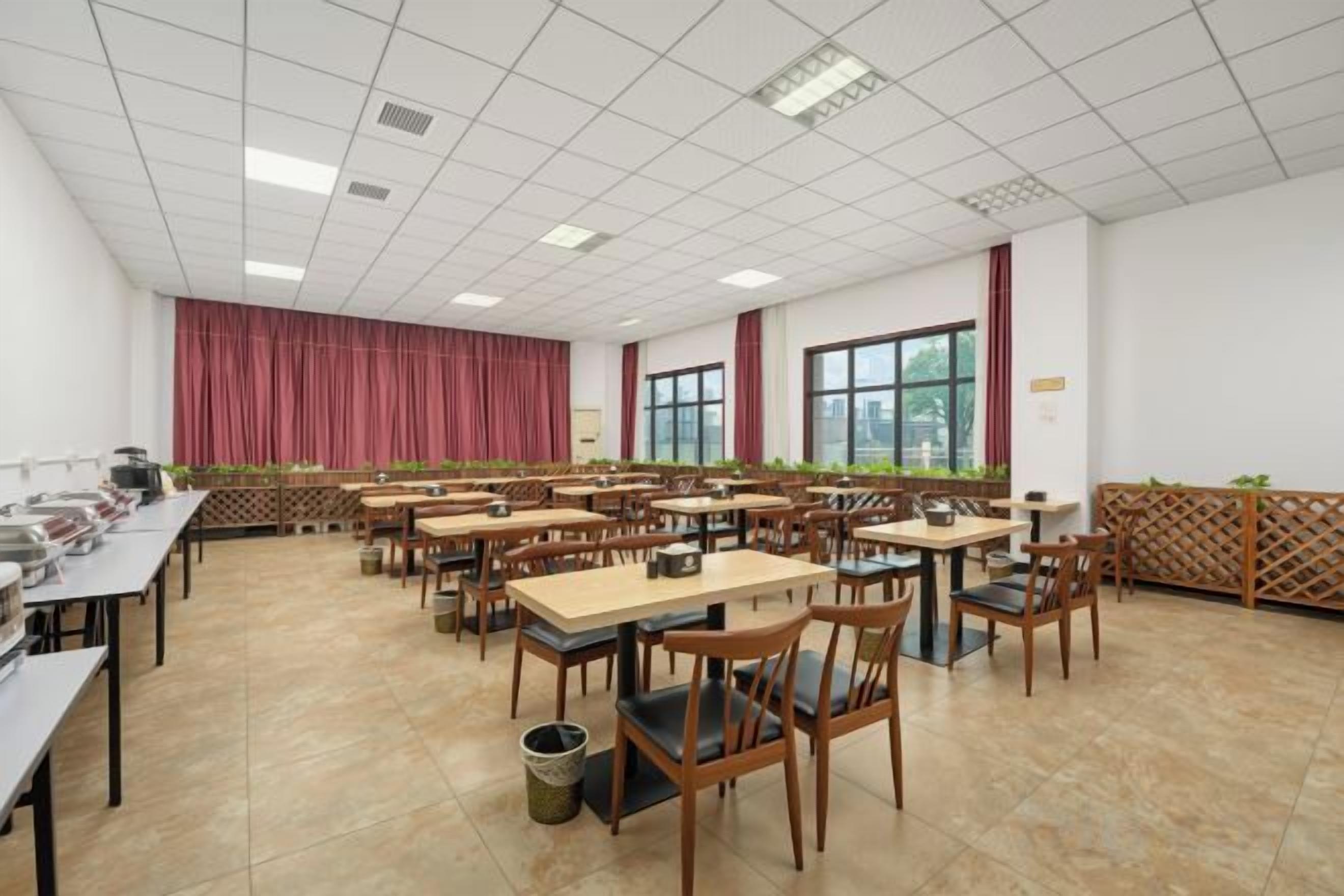 A conference room with multiple tables and chairs, large windows, and a red curtain backdrop.