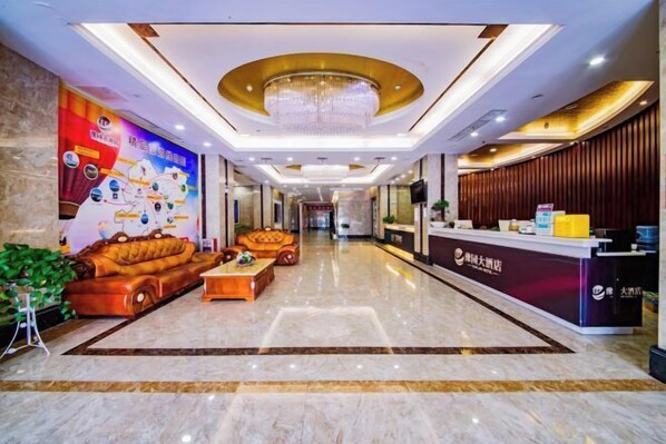 A hotel lobby with a reception desk, plush seating, a chandelier, and a large wall mural.