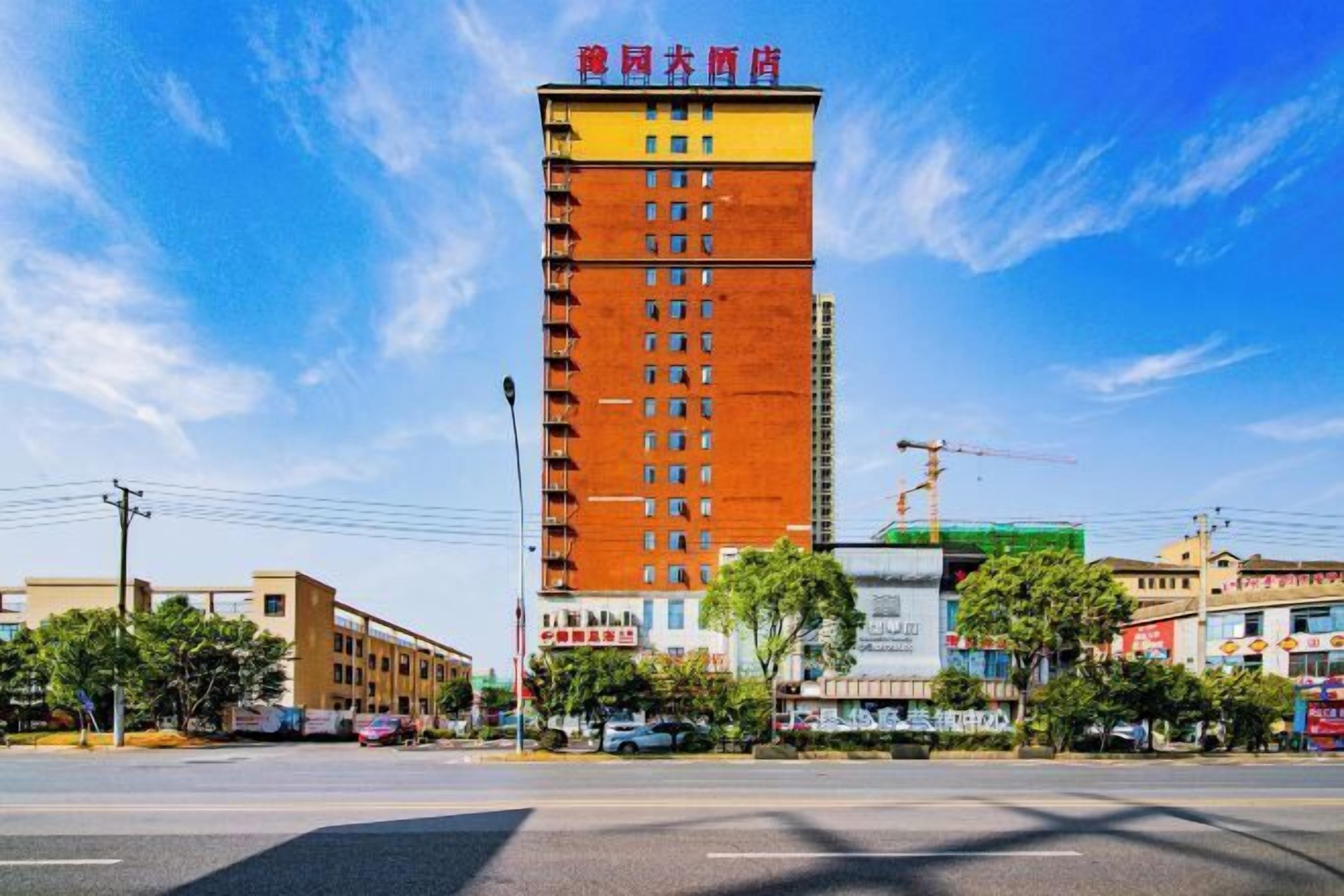 Un grand immeuble à étages, doté d’une façade rouge et jaune, qui ressemble probablement à un hôtel ou à un immeuble de bureaux, situé dans une rue bordée d’autres bâtiments commerciaux et de voitures garées.