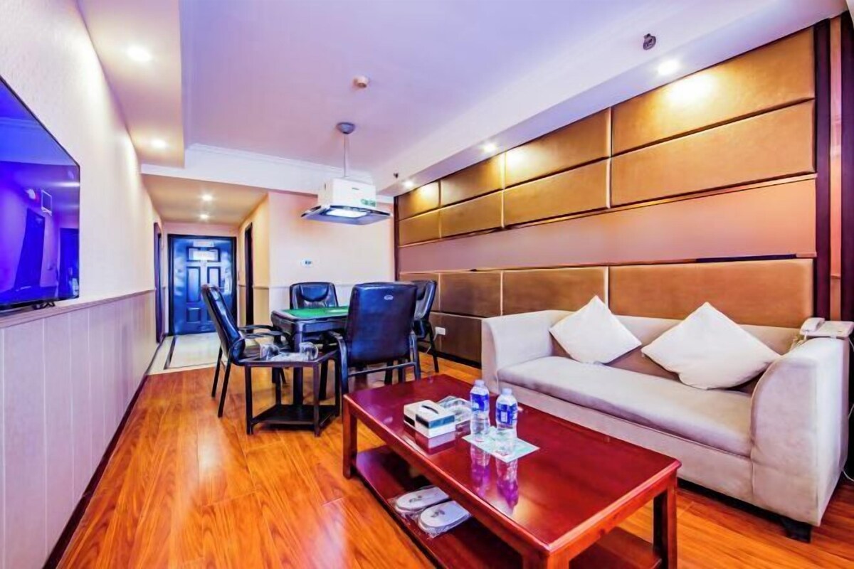 A hotel room with a wooden floor, a sofa, a coffee table, a desk with chairs, and a television.