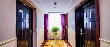 A hotel hallway with dark wooden doors, a patterned carpet, and a plant in the center.