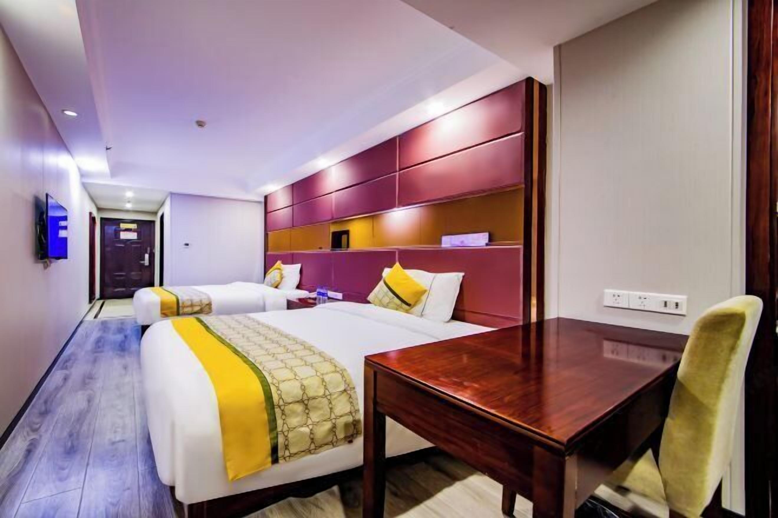 Habitación de hotel con dos camas, un escritorio de madera y una silla.