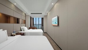 A hotel room with two beds, a TV, a desk, and a window with a view.