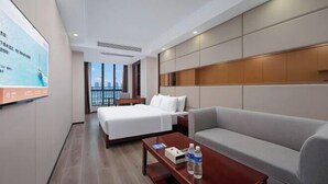 A hotel room with a bed, a sofa, a coffee table, and a TV screen.