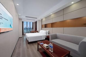 A hotel room with a bed, a sofa, a coffee table, and a TV screen.