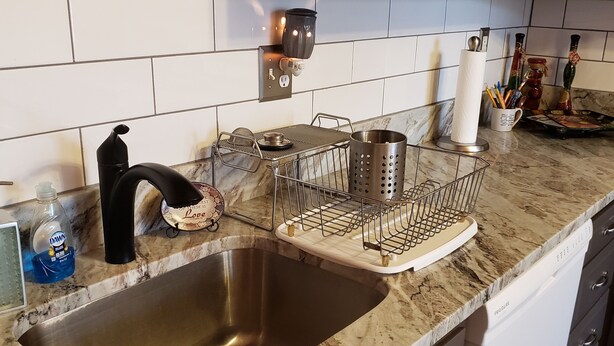 A kitchen with a stainless steel sink, marble countertop, and dark brown cabinets.