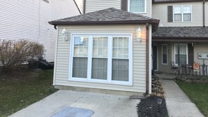 A small, single-story house with a large front window and two wall-mounted lights.