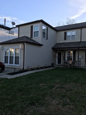 A two-story residential building with a garage, a covered patio, and a well-maintained lawn.