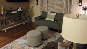 A living room with a sofa, ottomans, a TV, a lamp, and a decorative bowl on a table.