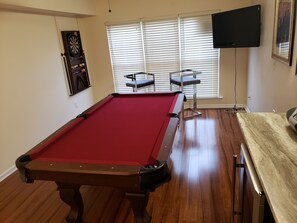 A pool table with a red felt surface, two pool cues, and a clock on the wall.