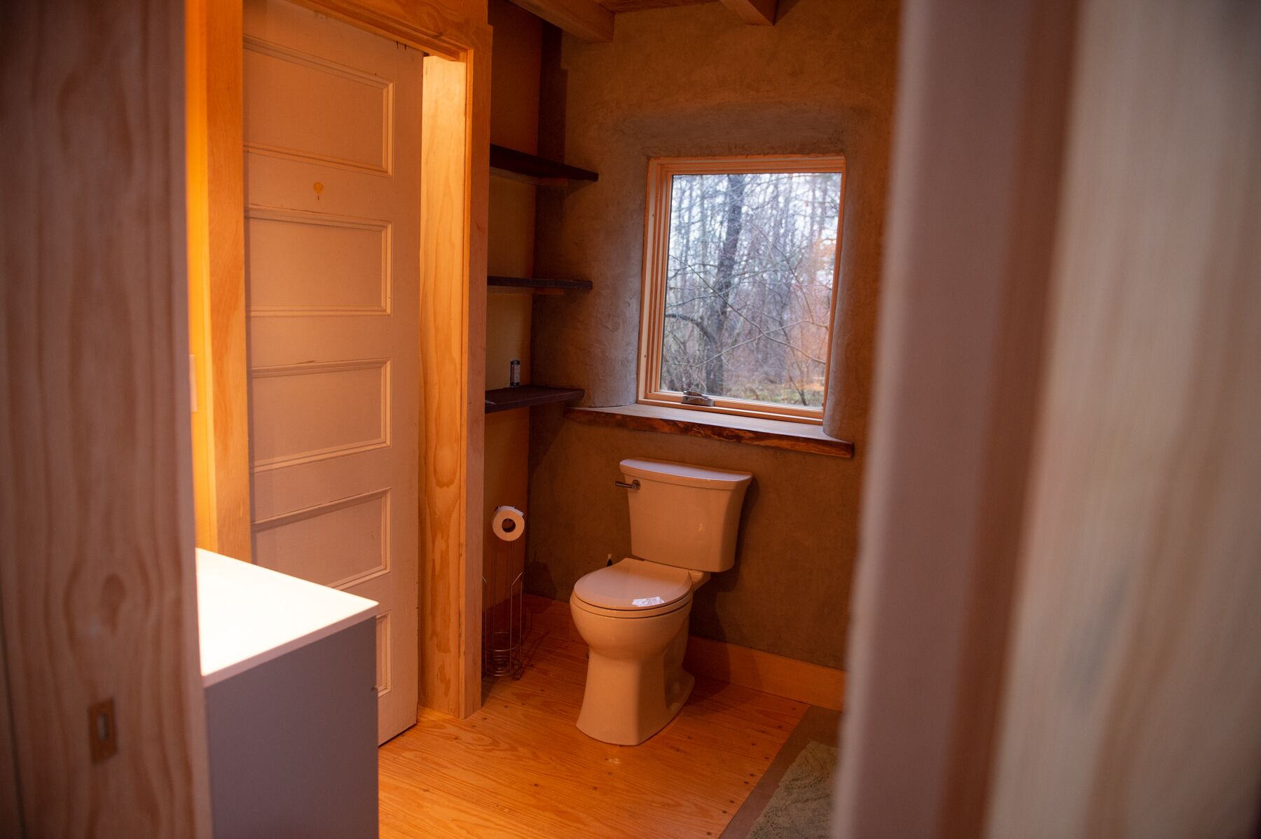 Une petite salle de bain comprenant des toilettes, une petite fenêtre et un plancher en bois.
