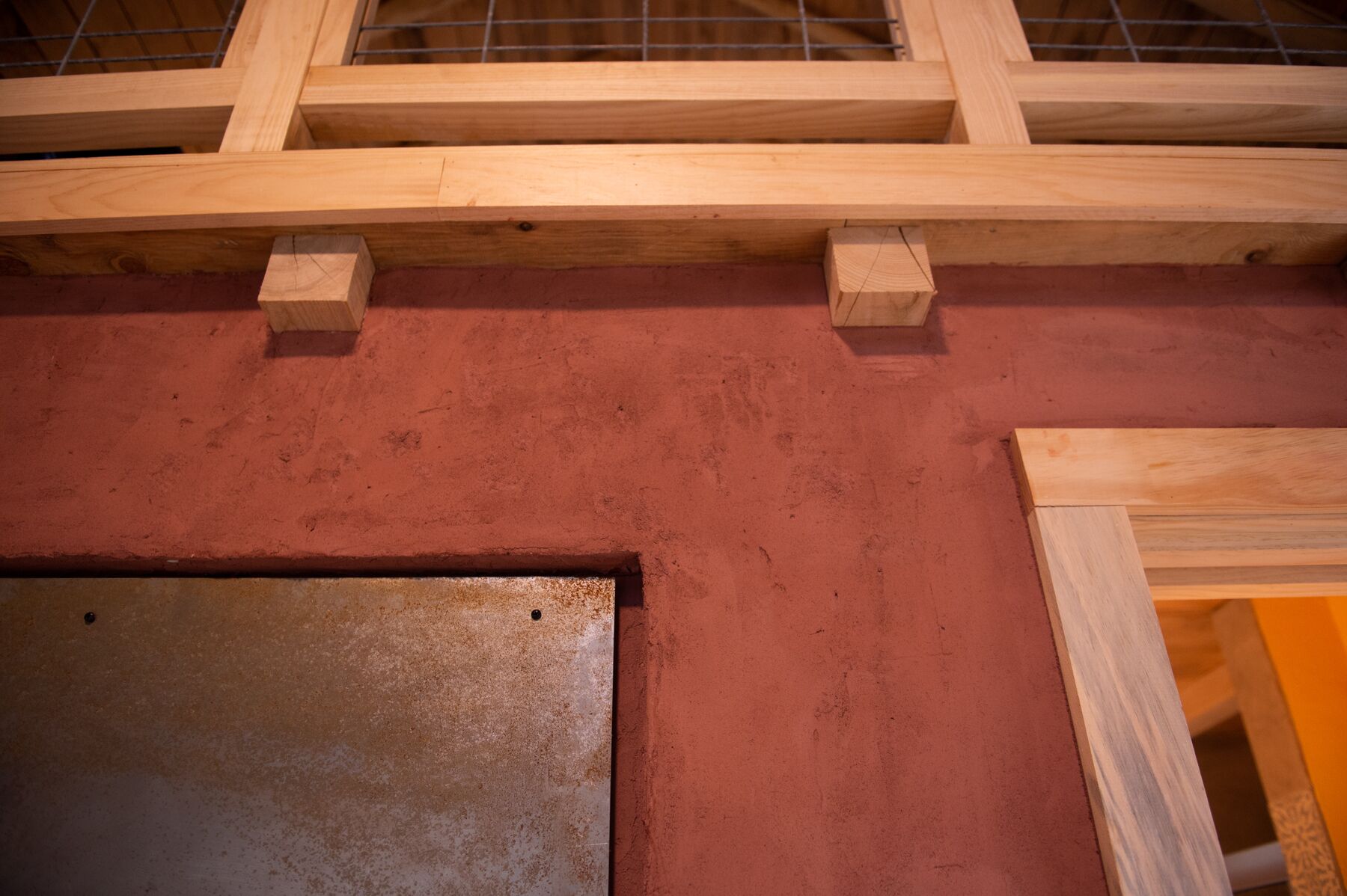 Una estructura de madera con un panel metálico y una pared roja.