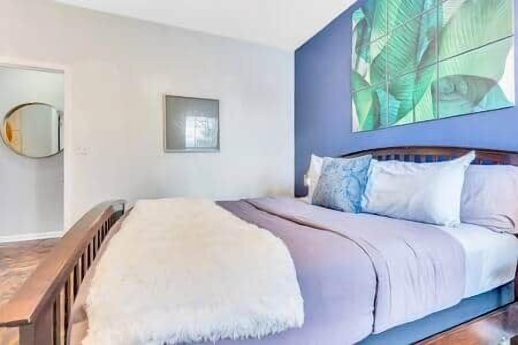 A bedroom with a bed, a wooden headboard, a window, and a wall-mounted mirror.