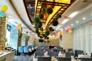 Une salle à manger d’hôtel avec de nombreuses tables et chaises, un plafond haut agrémenté d’un éclairage décoratif et un mur en pierre sur l’un des côtés.