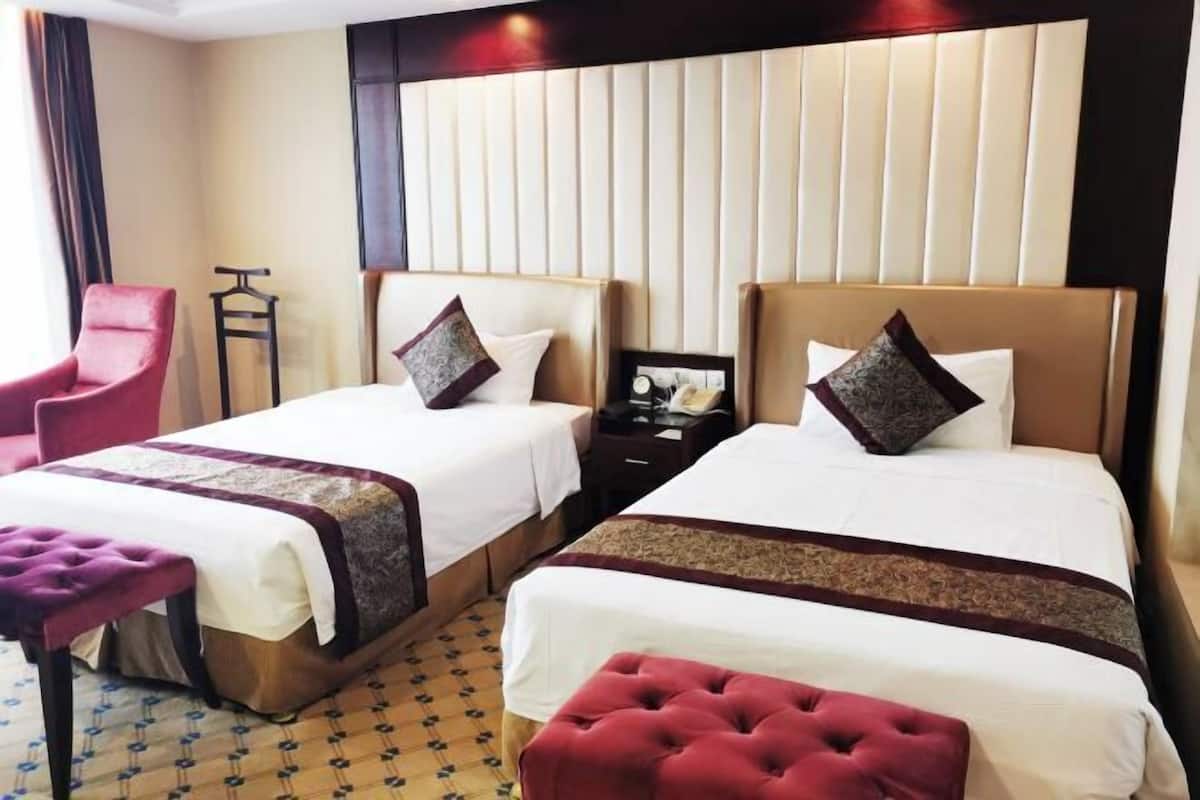 Una habitación de hotel con dos camas, un sillón rojo, una mesita y un suelo estampado.