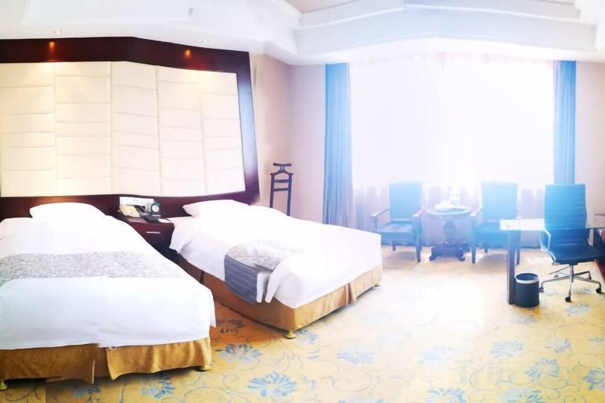 A hotel room with two beds, a desk, a chair, and a view of the outdoors.