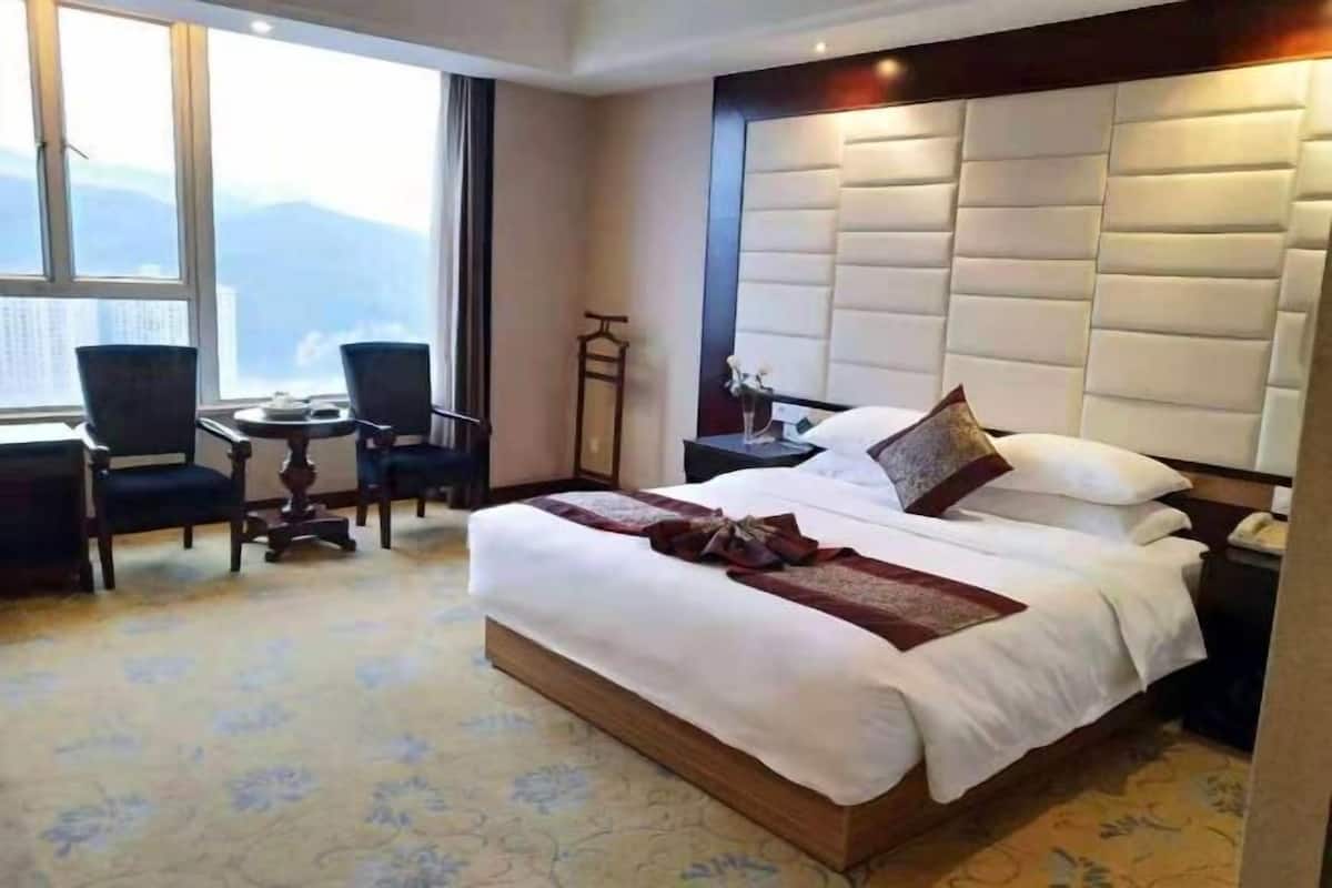Habitación de hotel con una cama grande, una mesita de noche, una silla, una pequeña mesa y vistas a las montañas a través de la ventana.
