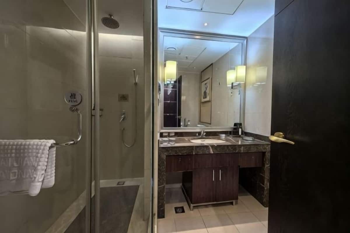Un baño con cabina de ducha de vidrio, un lavamanos con encimera oscura y un espejo sobre el lavamanos.