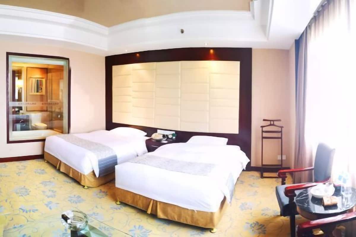Habitación de hotel con dos camas, una mesita pequeña, una silla y un espejo.