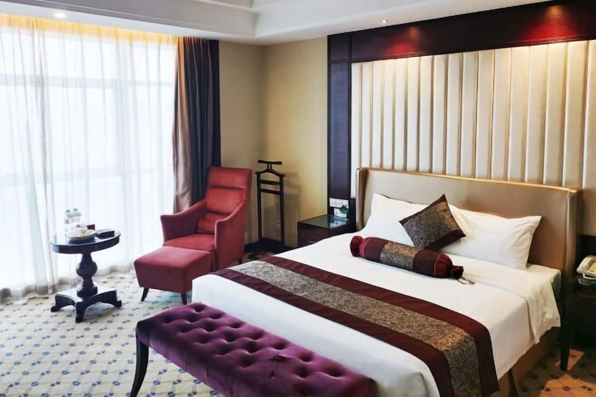 Una habitación de hotel con una cama grande, un sillón rojo, una mesita pequeña y un banco.