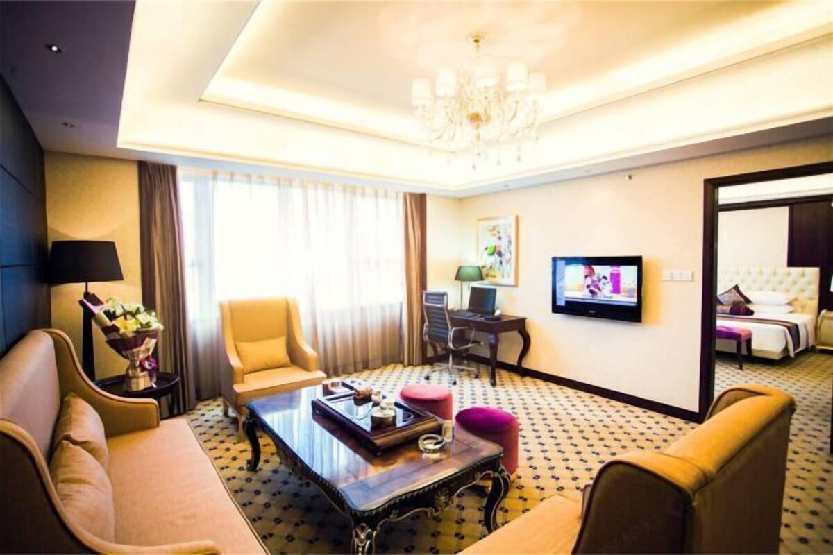 Habitación de hotel con sofá, sillón, mesa de centro, televisor, escritorio y cama.