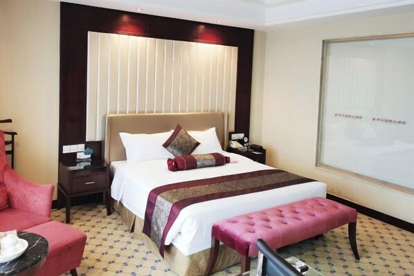 A hotel room with a large bed, a bedside table, a chair, a bench, and a large window. - Yanjiang International Hotel (Sanming)