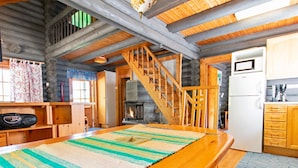 Interior acogedor de una cabaña con una mesa de comedor de madera, una chimenea, una zona de cocina y una escalera.
