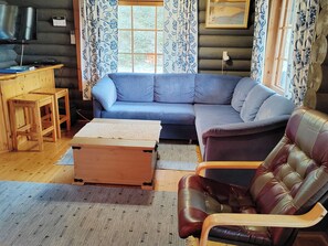 A cozy living room with a blue sofa, a wooden coffee table, a leather armchair, and a TV on a wooden stand.