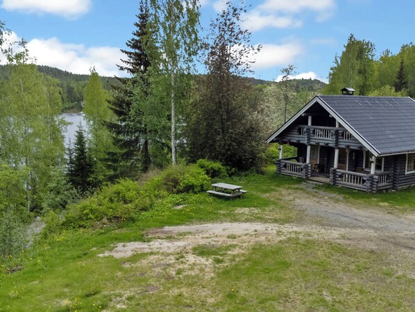 A cabin with a porch and a picnic table in a forested area with a river.