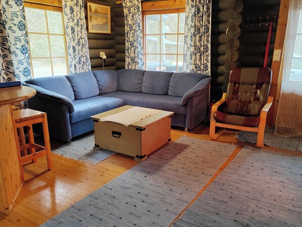 A log cabin interior with a blue sofa, a wooden chest, a guitar, and a chair.