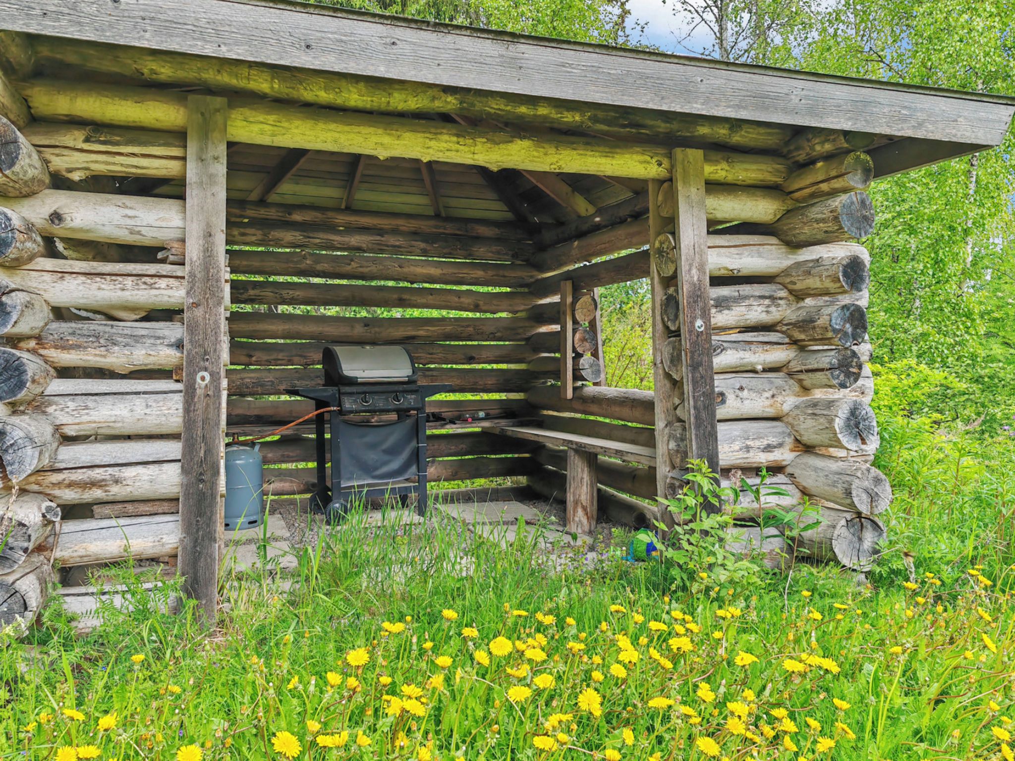 Une cabane en bois rustique, avec un barbecue et un distributeur d’eau à l’extérieur.