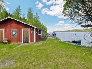 A red wooden building with a door and windows, a bench, and a clear view of a lake with boats. - Sinisorsa by Interhome (Joutsa)
