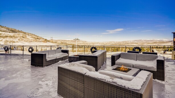 Eine Dachterrasse mit Gartenmöbeln und Feuerstelle mit Blick auf eine verschneite Landschaft.