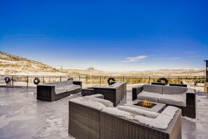 Une terrasse sur le toit, aménagée avec du mobilier d’extérieur et un foyer, offrant une vue sur un paysage enneigé.