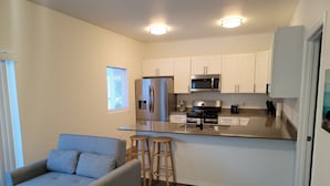 A modern kitchen with white cabinets, stainless steel appliances, and a grey sofa with wooden stools. - #204 New Beautiful Modern Condo Downtown Monroe! (Monroe)