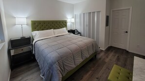 A bedroom with a green upholstered headboard, a bed with a grey quilt, two bedside tables with lamps, a wardrobe, and a door. - #204 New Beautiful Modern Condo Downtown Monroe! (Monroe)