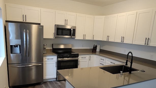 A modern kitchen with white cabinets, stainless steel appliances, and a large island with a sink. - #204 New Beautiful Modern Condo Downtown Monroe! (Monroe)