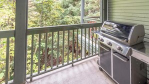 Ein Balkon mit Grill, Blick auf Bäume und eine Außenwand in Grün.